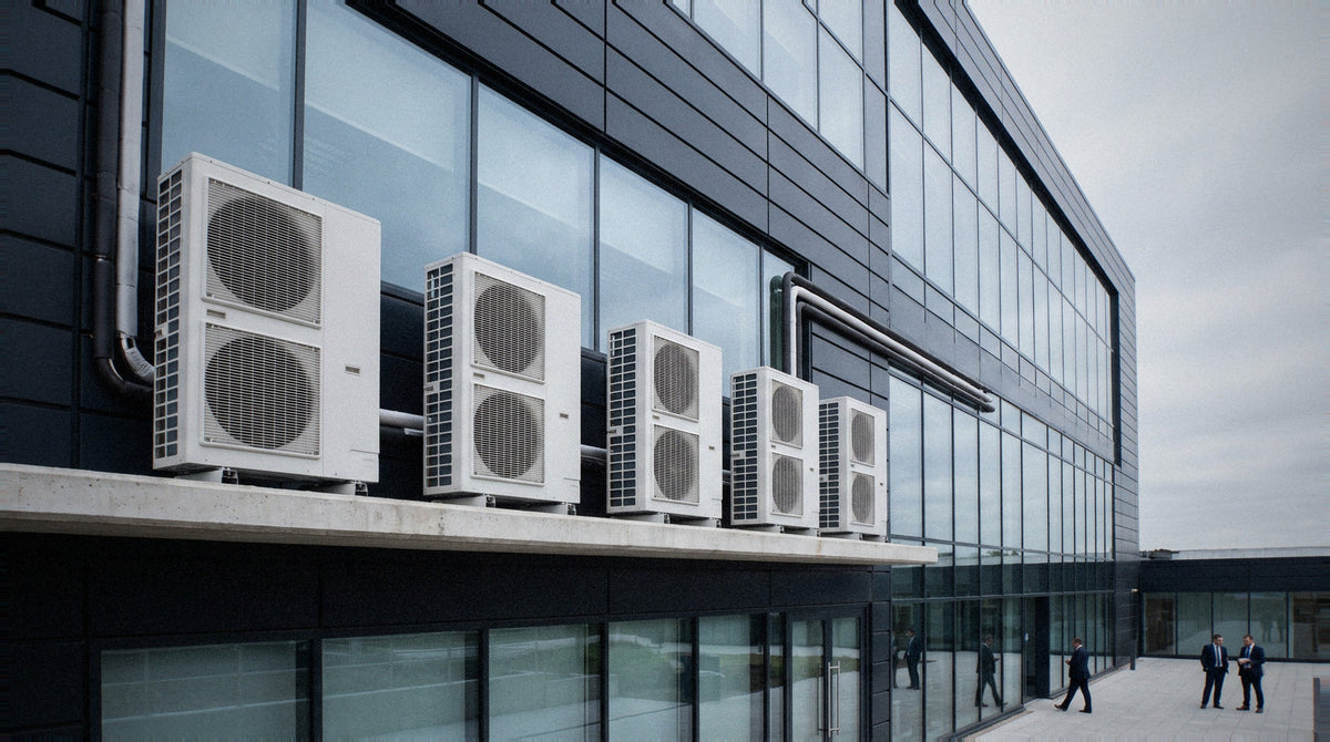 Row of large industrial air-conditioning chillers and condenser units on the rooftop of a British commercial building, with a hazy London office skyline in the background.