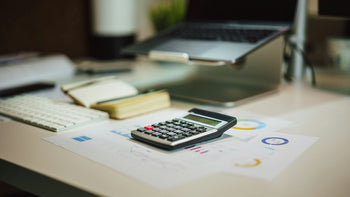 Calculator beside a laptop on a working desk