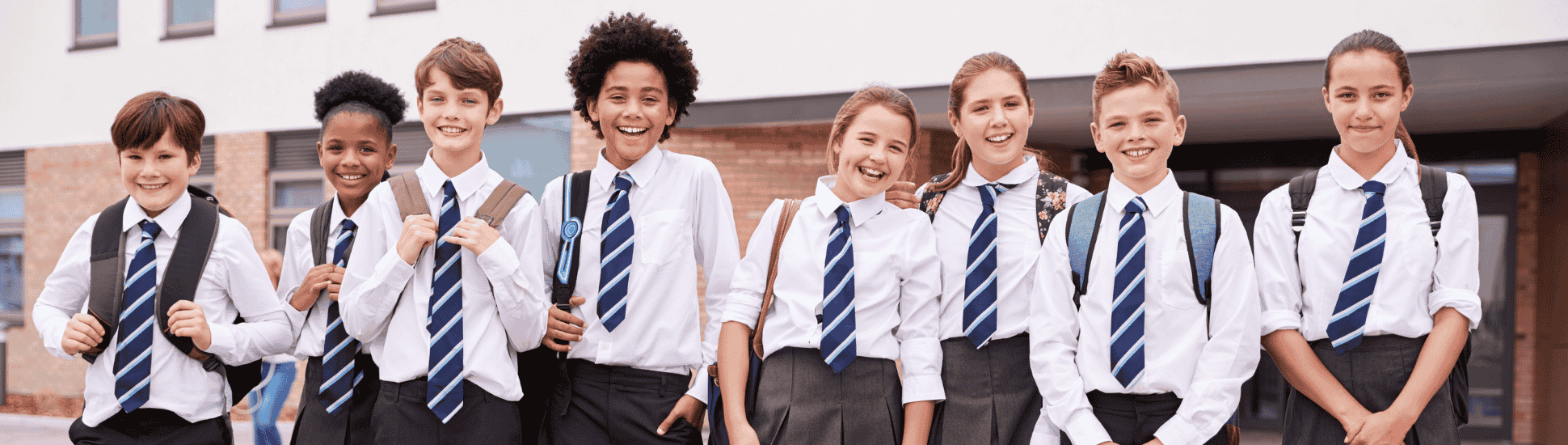 Group of UK secondary school students in uniform standing outside school building, smiling with backpacks